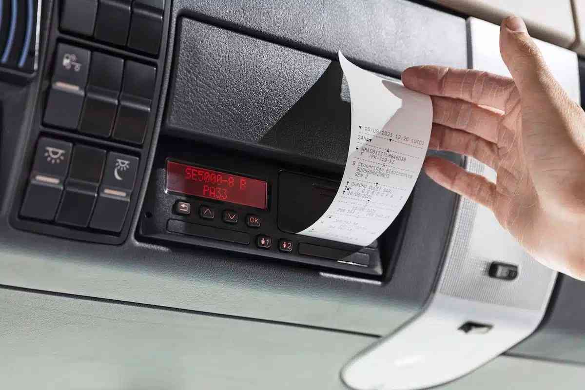 Main d'un chauffeur routier retirant un ticket imprimé d'un chronotachygraphe numérique sur le tableau de bord d'un camion.